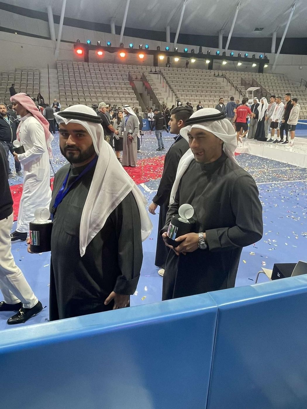 Naser in traditional dress holding a crystal award at a tennis arena